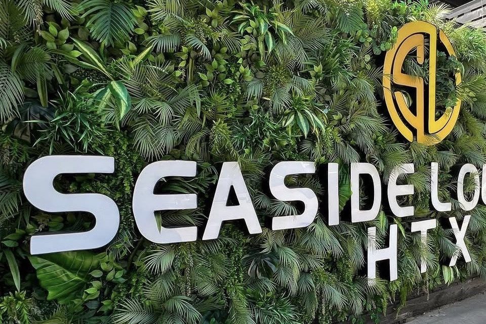 The Seaside Lounge HTX sign with its gold monogram on a living green wall